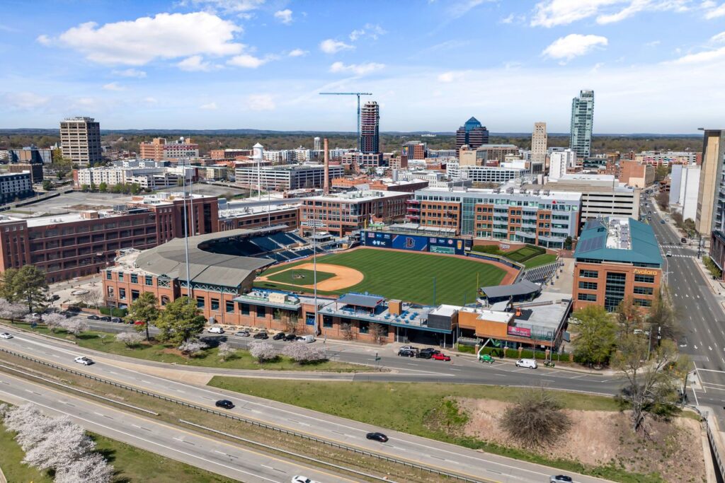 Aerial shot of Durham Bulls Athletic Park with city skyline in springtime